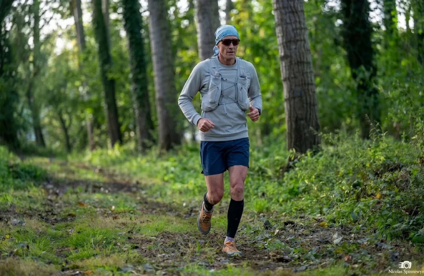 Runner amatoriale di mezza età corre su sentiero boschivo, simbolo di progressione e costanza nel lungo periodo.